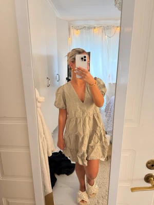 Zara Beige kort klänning med puffärm - Söt beige kortklänning med puffärmar och v-ringning. Klänningen har volangdetaljer och en avslappnad passform som ger en luftig känsla. Perfekt för varma dagar och enkel att styla med accessoarer. Tillverkad i ett lätt bomullsliknande material.