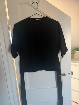 Svart t-shirt med knytband - Säljer en svart T-shirt med som knyts baktill. T-shirten är från Nelly i storlek S och är i fint skick.
