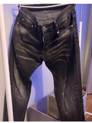 Svarta slitna jeans från Replay - Säljer ett par svarta jeans från Replay med slitningar och distressed detaljer. Jeansen har fem fickor, knappgylf och en slim fit passform. Materialet är denim med stretch för extra komfort. Perfekt för dig som gillar en cool och trendig look.
