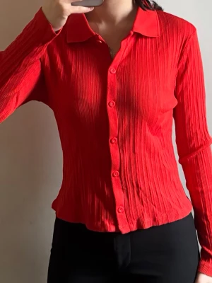 Röd långärmad skjorta med knappar - Säljer en snygg röd skjorta med långärmad design och klassisk krage från Gina Tricot. Skjortan har ett ribbat tyg och knappar hela vägen framtill. Perfekt för dig som vill sticka ut med en färgstark look. Storleken är L men passar även mig som är storlek XS-S. 
