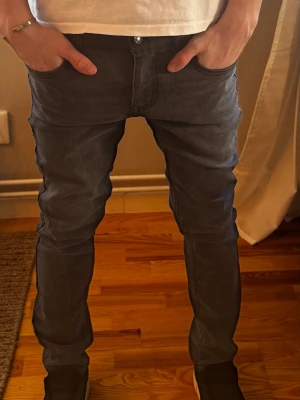 Grå slim fit jeans från Levi's - Snygga grå slim fit jeans i stl 14 från Levi's med klassiska fem fickor och diskreta sömmar. Jeansen har en modern passform som sitter tajt längs benen och är tillverkade i mjukt denimtyg. Perfekta för en trendig och avslappnad stil.