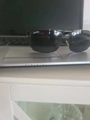 Svarta solglasögon från VEGOOS - Snygga svarta solglasögon från VEGOOS med rektangulära linser och metallbågar. De har en stilren design och mörka tonade glas som ger ett coolt uttryck. Perfekta för att skydda ögonen mot solen under sommaren.