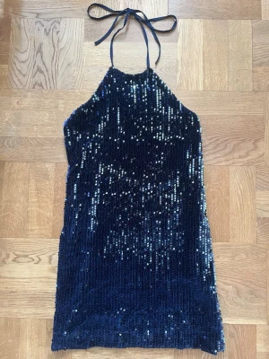 Mörkblå paljettklänning med öppen rygg - Mörkblå kortklänning täckt av blågröna paljetter. Halterneck-modell med knyt i nacken och öppen rygg. Klänningen är i storlek M. Har bara använt den 1 gång