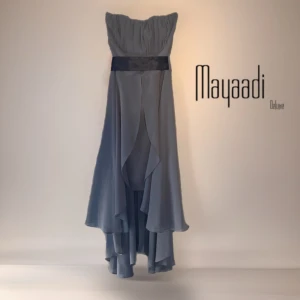 Grå axelbandslös långklänning ny med prislapp från Mayaadi - Snygg grå långklänning med axelbandslös design och ett brett svart band i midjan. Klänningen har ett elegant, flytande tyg med lager på lager-effekt och asymmetrisk nederkant som ger en cool och modern look.