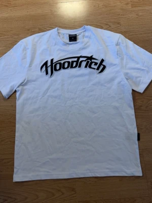 Vit Hoodrich t-shirt med tryck - Säljer en vit t-shirt från Hoodrich med stort svart logotryck på bröstet och flera grafiska tryck på ryggen. Klassisk rund hals och korta ärmar. Perfekt för dig som gillar streetwear och vill sticka ut med coola detaljer. Helt ny! Aldrig använd bara utan tagg!😁