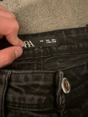 Svarta skinny jeans från Zara - Säljer ett par svarta skinny jeans från Zara med klassisk femficksdesign och knappgylf. Jeansen har en smal passform och är tillverkade i stretchigt denimtyg för extra komfort. Perfekta för en trendig och avslappnad look.