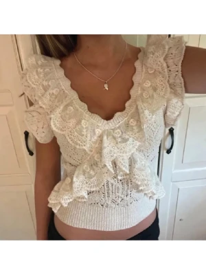 Zara topp med volanger - Supersöt vit blus med spetsdetaljer och volanger framtill. Djup v-ringning och korta ärmar med volangkant ger en romantisk vibe. Stretchig midja för skön passform. Perfekt för dig som gillar feminina och trendiga toppar.