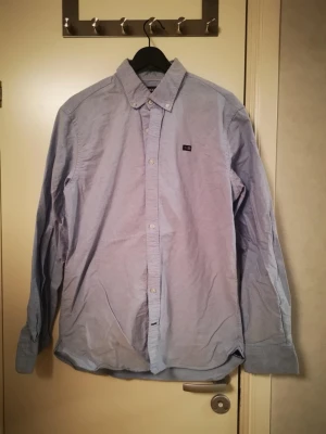 Blå skjorta från Sebago - Säljer en klassisk blå skjorta från Sebago med button-down krage och diskret logotyp på bröstet. Skjortan har långa ärmar och knappar hela vägen fram. Perfekt för dig som gillar en enkel och stilren look.