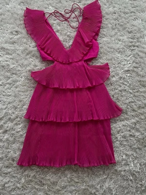 Rosa volangklänning från ASOS  - Supersnygg rosa kortklänning från ASOS DESIGN. Den är lite öppen i midjan, har plisserade volanger och djup v-ringning och öppen i ryggen. Snören finns så att man kan knyta den så att den inte glider ner på axlarna. Pris kan diskuteras💕