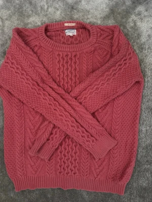  kabelstickad tröja gant - Säljer en snygg kabelstickad tröja från Gant i en varm rosa färg. Tröjan har rund halsringning, ribbade muddar och ett klassiskt flätmönster över hela plagget. Perfekt för dig som gillar en tidlös och mysig stil.
