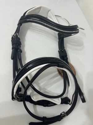 Svart och vitt träns med strass - Snyggt träns i svart och vitt läder med mjuk vaddering och strassdetaljer på pannbandet. Tränset har anatomisk form och justerbara spännen. Perfekt för dig som vill ha något extra :-)
