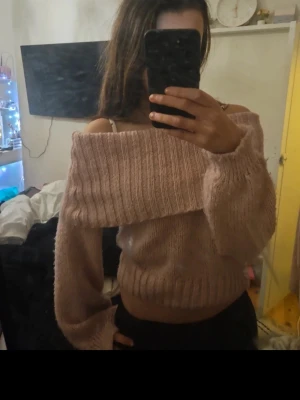 Ljusrosa off shoulder stickad tröja - Säljer en ljusrosa stickad tröja med bred off shoulder-krage och långa, lite pösiga ärmar. Tröjan är kortare i modellen och har ribbstickade detaljer vid kragen och nederkanten. Perfekt för dig som gillar en avslappnad och trendig look.