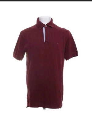 En fin Vinröd piké T-Shirt från Tommy Hilfiger - En fin T-shirt från Tommy Hilfiger. Väldigt bra skick dock tror att en knapp är borta som syns på bilden😉  Vid frågor är det bara att ni hör av er🤗