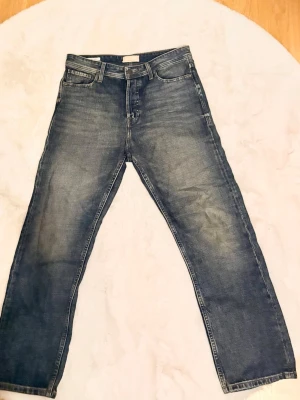 Blå raka jeans med tvättad look - Säljer ett par blå jeans med rak passform och snyggt tvättad finish. Jeansen har klassisk femficksdesign, normal midja.