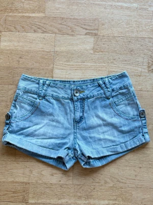 Lågmidjade ljusblå jeansshorts - Lowwaist ljusblå jeansshorts med knappdetaljer på sidorna. Snygg detalij på baksidan, inga bakfickor. Perfekta till sommaren och lätta att matcha med olika toppar. Köpta här på Plick men passade tyvärr inte mig. Fråga om mått❣️