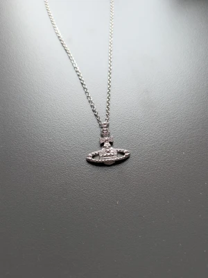 Vivienne Westwood silverhalsband - Säljer ett snyggt silverfärgat halsband från Vivienne Westwood med ikonisk orb-berlock dekorerad med små gnistrande stenar. Kedjan är tunn och elegant, och halsbandet kommer med original ask och tygpåse.