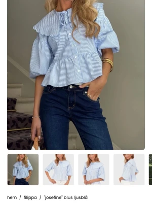 Ljusblå Josefine blus från Filippa - Ljusblå blus med vita ränder från Filippa, modell Josefine. Blusen har en stor krage med volangkant, knappar framtill och puffiga trekvartsärmar. Materialet är lätt och luftig bomull, perfekt för en trendig och avslappnad look. Med prislapp