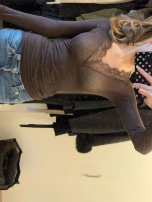 Intimissimi tröja - Snygg brun långärmad topp med v-ringning och dekorativ spetsdetalj vid halsen. Perfekt att matcha med jeans eller kjol för en trendig look. Toppens passform är tight och materialet känns mjukt mot huden.