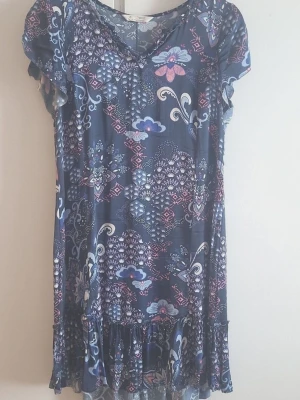 Odd Molly klänning med blommigt mönster - Mönstrad klänning med volang nedtill. Klänningen har ett vackert mönster i blåa och rosa toner. Kortärmad modell. Klänningen är kortare framme och längre bak. Storlek 2 ( M ) i jättefin skick. Mått: längd fram 84, bak 93cm.  armh-armh 50cm.