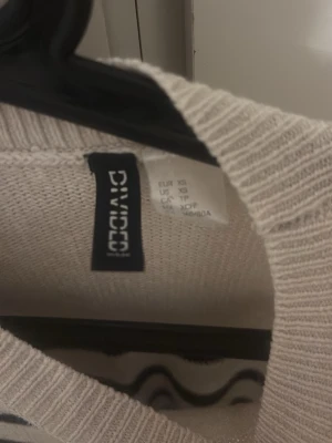 Randig stickad tröja från DIVIDED - Stickad tröja från DIVIDED i storlek XS. Tröjan är cremevit med svarta horisontella ränder, har rund hals och långa ärmar. Materialet är mjukt och lätt, perfekt för lager-på-lager och en chill look.
