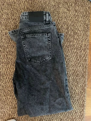 Svarta jeans från Grunt - Säljer ett par svarta  jeans från Grunt i tvättad look. Jeansen har hög midja, raka ben och klassiska bakfickor. Tillverkade i ekologisk bomull för en skön och hållbar känsla. Perfekta till en avslappnad stil.