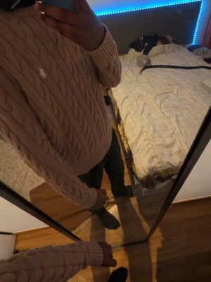 Beige kabelstickad tröja Polo Ralph Lauren - Säljer en beige kabelstickad tröja från Polo Ralph Lauren med klassisk rund halsringning och ribbade muddar. Tröjan har den ikoniska vita logon broderad på bröstet och är tillverkad i mjukt material. Perfekt för dig som gillar stilrena och tidlösa plagg.