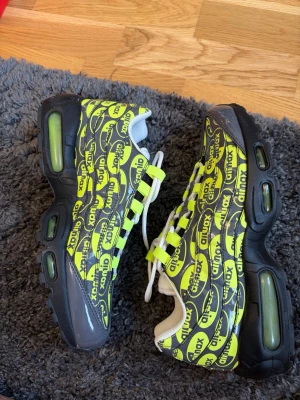 Nike Air Max 95 gul/svart sneakers - Nike Air Max 95 sneakers med svart och neon-gul färgkombination. Skorna har ett mönster med 'air max'-loggor över hela ovandelen, vita skosnören och synliga Air-enheter i sulan. Ovandelen är i textil och syntet, och sulan är svart med neon-detaljer. No box
