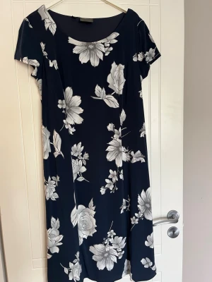 Marinblå blommig klänning från bpc - Snygg marinblå klänning från bpc med vita blommor. Klänningen har korta ärmar och en rund halsringning. Den är lätt figursydd och har ett elegant blommigt mönster som ger en fräsch look. Perfekt för sommarens alla tillfällen.