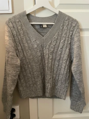 Grå tröja med v-ringning - Säljer en grå tröja från H&M med v-ringad hals och ribbade muddar. Tröjan har ett klassiskt mönster och är långärmad, perfekt för att hålla sig varm under kyliga dagar. Materialet är mjukt och bekvämt. 