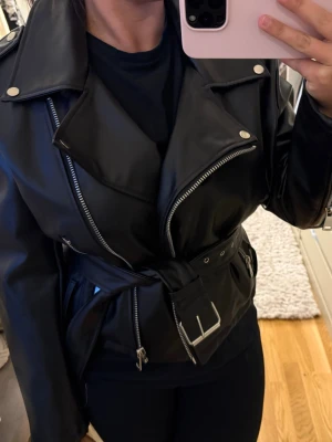 Svart biker skinnjacka med bälte - Säljer min oversized skinnjacka! Jackan är i god skick då den endast är andvänd vid två tillfällen. Jackan tillkommer med ett bälte som man kan välja att knyta runt midjan eller ta bort☺️💕