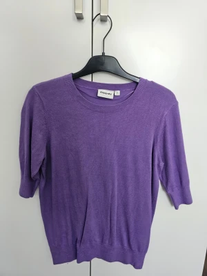 Lila stickad tröja från Kappahl - Lila stickad tröja från Kappahl med rund halsringning och halvlånga ärmar. Tröjan har en enkel och stilren design med ribbstickade detaljer vid hals, ärmslut och nederkant. Perfekt för att addera lite färg till din outfit.