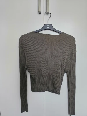 Olivgrön ribbstickad tröja - Säljer en olivgrön ribbstickad tröja med lång ärm och croppad passform. Tröjan har ett snyggt geometriskt mönster i stickningen och rund halsringning. Perfekt för dig som gillar stilrena och trendiga plagg.