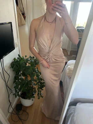 Beige balklänning i satin - Säljer denna jättefina balklänning som endast använts en gång och därmed är i nyskick. Så snygg framtill och fantastisk baktill med dom hängande banden som även kan knytas till rosett ifall man vill(bild 4). 