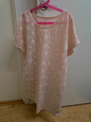 Ljusrosa oversized t shirt med stjärnmönster halv see-through  - Mysigt ljusrosa t-shirt med vita stjärnor framtill. Den har en lös passform, korta ärmar och rund halsringning. Halv see-through. Nytt, aldrig använt.