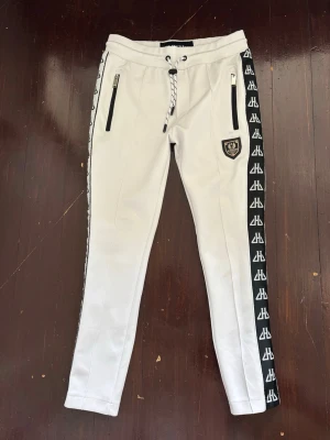 Vita track pants med svarta detaljer - Track pants ifrån Horspist med svarta sidopaneler och logga längs benen. Byxorna har dragsko i midjan, två dragkedjefickor framtill och ett Horspist märke på låret. 