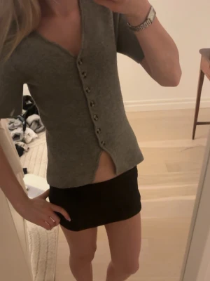 Grå kortärmad kofta från Gina Tricot - Kortärmad grå kofta från Gina Tricot med v-ringning och knappar framtill.