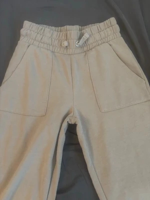 Beige mjukisbyxor med resårmidja - Snygga beige mjukisbyxor med bred resår i midjan. Byxorna har stora fickor ock är perfekta för en avslappnad och chill stil.