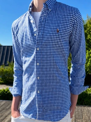 Blårutig skjorta från Ralph Lauren - Blå vit rutig(MODELLEN ÄR 185CM OCH VÄGER 75KG)Klassisk blårutig skjorta från Ralph Lauren med button-down krage och broderad logga på bröstet. Skjortan har lång ärm, vita knappar och är tillverkad i bomull. Perfekt för en stilren och avslappnad look.