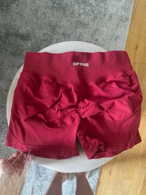 Röda seamless träningsshorts DFYNE - Säljer ett par röda seamless träningsshorts från DFYNE. De har hög midja, ribbad linning och scrunch-detalj bak. Materialet är stretchigt och passar perfekt för gym eller annan träning. Snygg och bekväm passform.