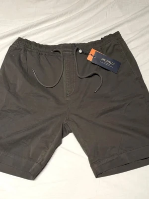 Morris mörkgröna shorts med snörning - Stilrena mörkgröna shorts från Morris med elastisk midja och snörning. Shortsen har sidofickor och bakfickor med knapp, perfekta för sommardagar. Tillverkade i mjuk bomull för en skön känsla och avslappnad look.