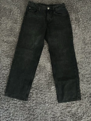 Svarta raka jeans från H&M - Säljer ett par svarta raka jeans från H&M med klassisk femficksmodell och knappgylf. Jeansen har en enkel och stilren look som passar till allt och är tillverkade i bomull. Perfekta för dig som gillar en avslappnad men snygg stil.