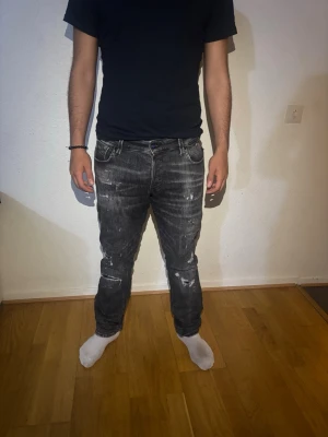 Svarta jeans Jack & Jones - Säljer ett par svarta slim fit jeans från Jack & Jones, modell Glenn. Jeansen har en tvättad look med slitningar och vita detaljer för en cool, avslappnad stil. Klassisk femficksmodell och stretchigt material för extra komfort.