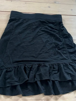 Svart kjol med volangkant - En svart kort kjol i mjukt tyg med bred linning och volangkant längst ner. Kjolen har en enkel, klassisk form och passar perfekt till många olika stilar. Materialet känns som bomull och modellen är normal i passformen. Använd 2 ggr. Från gina tricot