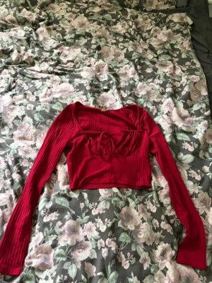 Röd croppad topp från Nelly - Trendig röd croppad topp från Nelly med långa ärmar och ribbad struktur. Toppen har en snygg snörningsdetalj framtill och en figurnära passform som framhäver midjan. Perfekt för dig som vill ha en statement piece i garderoben.