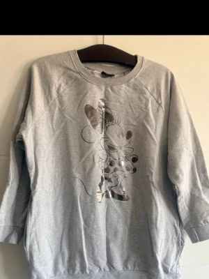 🩶✨ Damhoodie Minnie Mouse – grå med fickor ✨🩶 - 🩶✨ Damhoodie Minnie Mouse – grå med fickor ✨🩶  🌸 Säljer en damhoodie i grå färg med Minnie Mouse. På framsidan finns en silverfärgad Minnie-figur. Hoodien har dessutom fickor, vilket gör den både praktisk och bekväm. Perfekt för vardagsbruk 💕  👚 Storlek: L 🏷️ Märke: Minnie Mouse  📏 Mått: 📐 Bredd: 110 cm 📏 Längd: 71 cm  ✨ Mycket bra skick – använd max ca 5 gånger.  💌 Hör gärna av dig om du har frågor. Välkommen att köpa! 😊 