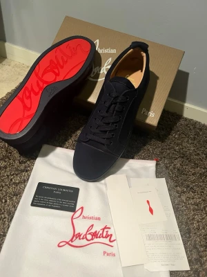 Blåa skor från Christian Louboutin - Stilrena svarta sneakers från Christian Louboutin med klassisk röd sula och ovandel i mocka. Skorna har svarta skosnören, diskret design och lågt skaft. Kommer med originalkartong och dustbag.