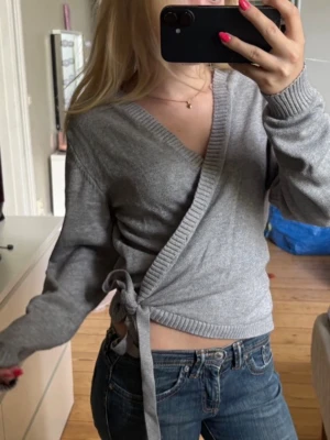 Grå omlottkofta med knytband - Snygg grå omlottkofta med knytband i sidan och ribbade kanter. Koftan har V-ringning och långa ärmar, perfekt att styla med jeans eller kjol för en chill look🧘🏼‍♀️