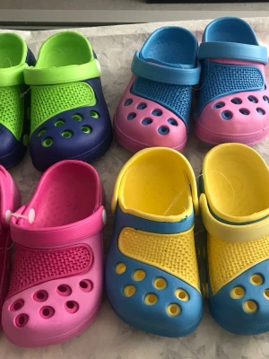 Färgglada Barn sandaler  - Säljer flera par barn sandaler med hålmönster och justerbar hälrem. Finns i olika färgkombinationer som rosa, blå, gul, grön och lila. Perfekta för sommaren och lätta att ta på. Sköna att använda både inne och ute. Stlk kvar24-28 . 85kr/par , helt ny 