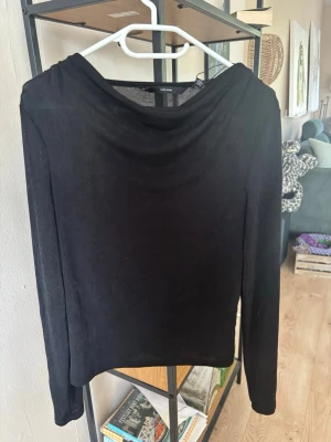 Svart långärmad topp Vero Moda - Stilren svart långärmad topp från Vero Moda med lätt draperad halsringning. Tillverkad i ett tunt, mjukt material som känns bekvämt mot huden. Perfekt att matcha med jeans eller kjol för en trendig look. Använd en gång. 