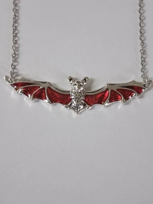 Halsband med fladdermus i silver och rött - Unikt halsband med en fladdermus i silverfärgad metall och röd legering detaljer på vingarna. Kedjan är tunn och smidig, och fladdermusen har en cool, detaljrik design som sticker ut. Materialet rostfritt stål. 